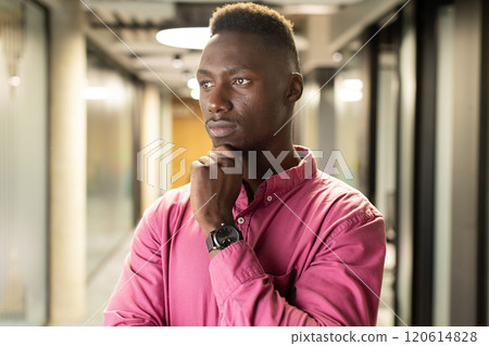 Thinking deeply, african american man in pink shirt standing in modern office hallway Thinking deeply, african american man in pink shirt standing in modern office hallway 120614828