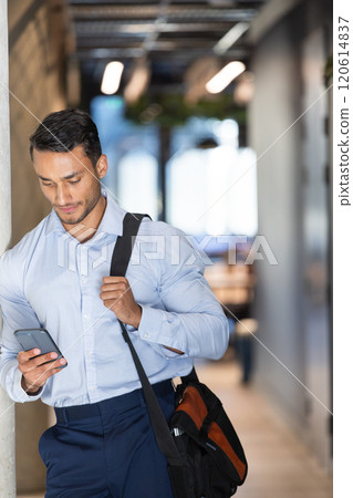 Business professional holding smartphone and carrying bag, walking in office hallway 120614837