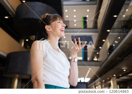 Smiling businesswoman using smartphone for voice message in modern office building Smiling businesswoman using smartphone for voice message in modern office building 120614865