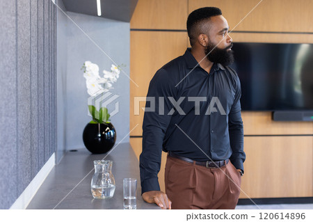 Standing in office, business professional looking thoughtful with water pitcher and glass 120614896
