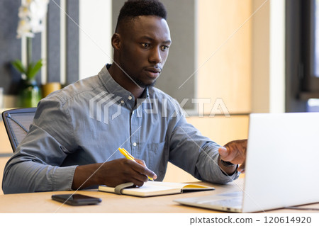 Working on laptop, man taking notes in office, focusing on task 120614920