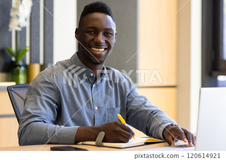 Smiling african american businessman writing in notebook at desk with laptop and smartphone 120614921