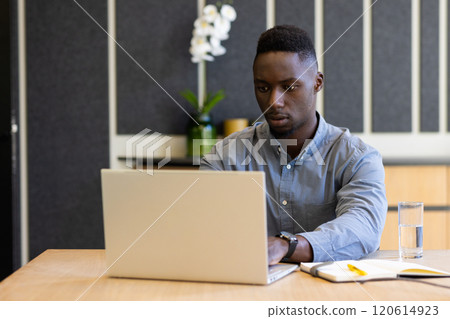 Working on laptop, man focusing on tasks with notebook and glass of water nearby 120614923