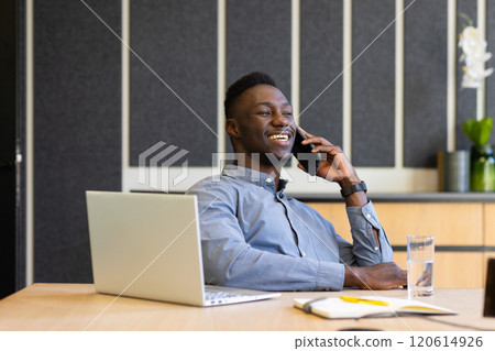 Talking on smartphone, man smiling and working on laptop at office desk Talking on smartphone, man smiling and working on laptop at office desk 120614926