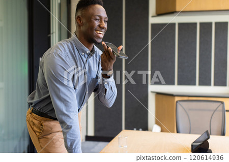 Speaking into smartphone, man standing in modern office, smiling and working 120614936