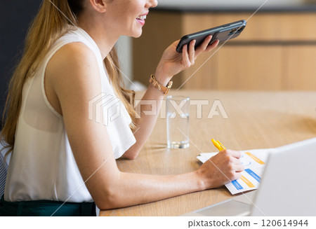 Holding smartphone and writing notes, woman working at office desk, copy space 120614944