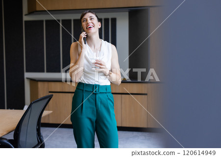 Talking on smartphone and holding glass of water, woman smiling in office Talking on smartphone and holding glass of water, woman smiling in office 120614949