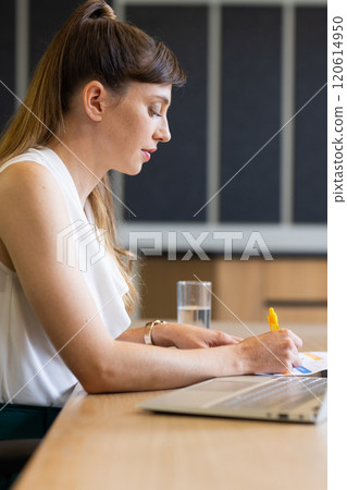 Writing notes, woman working at desk with laptop and glass of water Writing notes, woman working at desk with laptop and glass of water 120614950