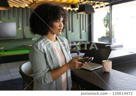 Using smartphone, businesswoman standing by counter with laptop and coffee mug Using smartphone, businesswoman standing by counter with laptop and coffee mug 120614972
