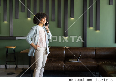 Talking on smartphone, woman standing in modern office with laptop on couch, copy space Talking on smartphone, woman standing in modern office with laptop on couch, copy space 120615000