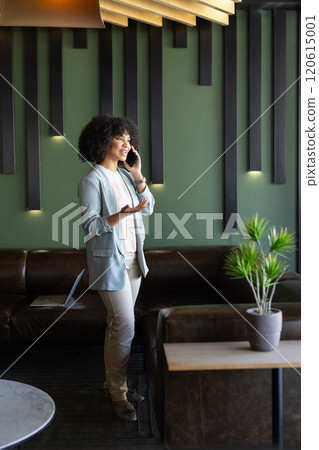 Talking on smartphone, businesswoman standing in modern office with laptop nearby 120615001