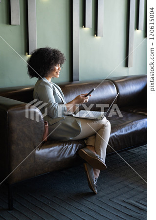 Using smartphone and laptop, woman working on couch in modern office Using smartphone and laptop, woman working on couch in modern office 120615004