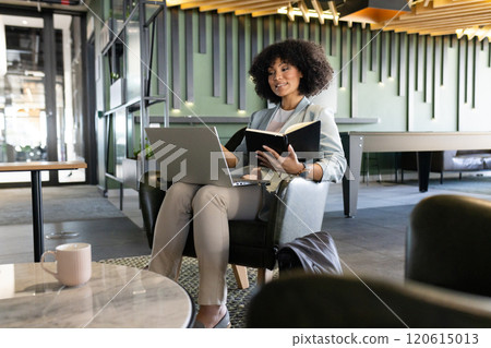 Working in modern office, woman using laptop and reading notebook, smiling Working in modern office, woman using laptop and reading notebook, smiling 120615013