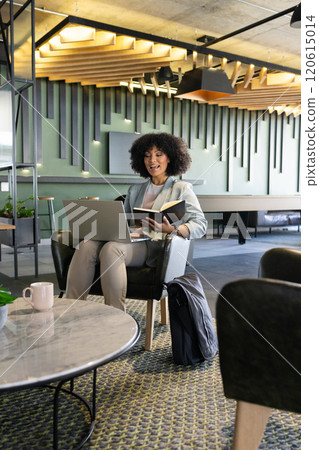 Holding laptop and notebook, woman working in modern office lounge area 120615014