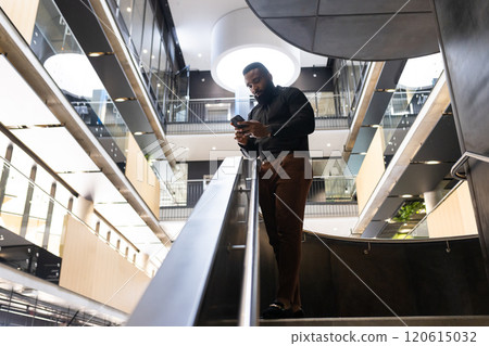Businessman using smartphone while walking down stairs in modern office building, copy space 120615032