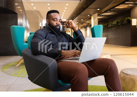 Using laptop and talking on smartphone, African american man working in modern office setting Using laptop and talking on smartphone, African american man working in modern office setting 120615044
