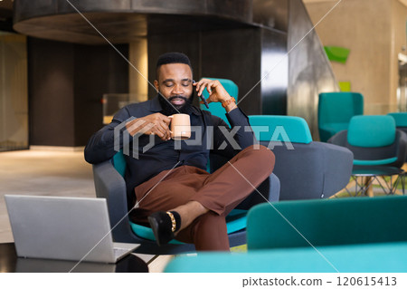 Talking on phone and drinking coffee, businessman working on laptop in office 120615413