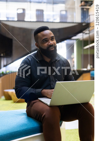 Working on laptop, African american man sitting in modern office, focusing on tasks 120615419