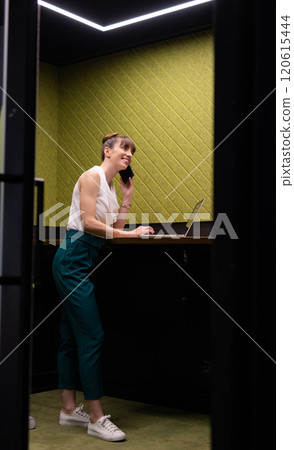 Talking on smartphone, woman working on laptop in modern office space Talking on smartphone, woman working on laptop in modern office space 120615444