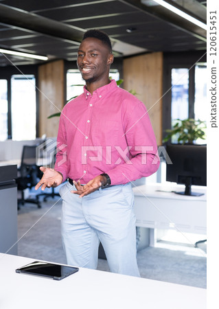 Smiling businessman in office, gesturing while standing near tablet on desk Smiling businessman in office, gesturing while standing near tablet on desk 120615451