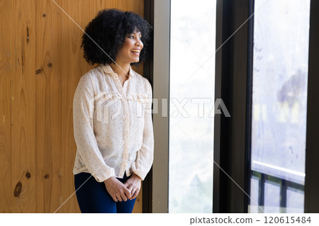 Smiling woman standing by window, wearing polka dot blouse, looking outside 120615484
