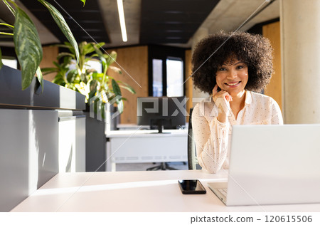 Smiling woman working on laptop with smartphone on desk in modern office, copy space Smiling woman working on laptop with smartphone on desk in modern office, copy space 120615506