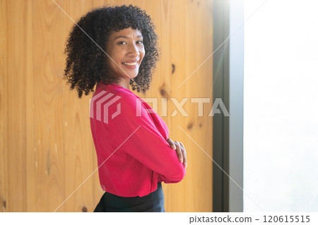 Smiling businesswoman in red blouse standing with arms crossed in office Smiling businesswoman in red blouse standing with arms crossed in office 120615515