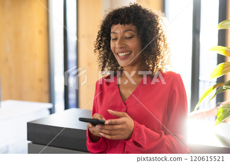 Smiling woman using smartphone in modern office, wearing red blouse 120615521