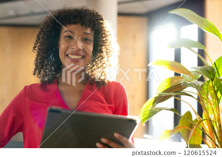 Smiling businesswoman holding tablet, standing near plant in modern office Smiling businesswoman holding tablet, standing near plant in modern office 120615524