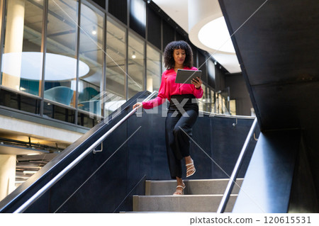 Businesswoman walking down stairs using tablet in modern office building Businesswoman walking down stairs using tablet in modern office building 120615531