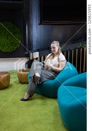 Using smartphone, businesswoman sitting on bean bag chair in modern office Using smartphone, businesswoman sitting on bean bag chair in modern office 120615955