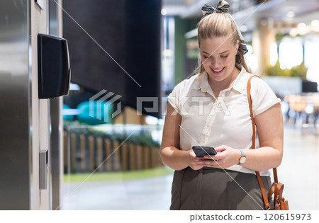 Using smartphone, businesswoman smiling while standing in modern office lobby Using smartphone, businesswoman smiling while standing in modern office lobby 120615973