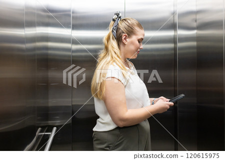 At office, Using smartphone, businesswoman in elevator, focusing on screen At office, Using smartphone, businesswoman in elevator, focusing on screen 120615975