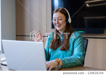 Waving and smiling, woman using laptop and wearing headphones in office 120616144
