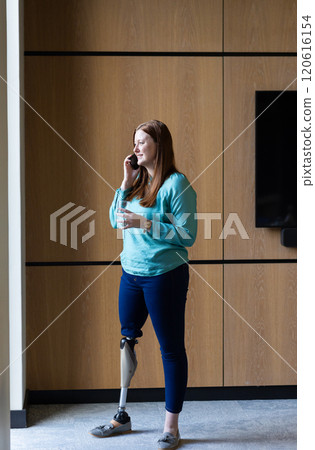 Talking on smartphone, woman with prosthetic leg standing in modern office Talking on smartphone, woman with prosthetic leg standing in modern office 120616154