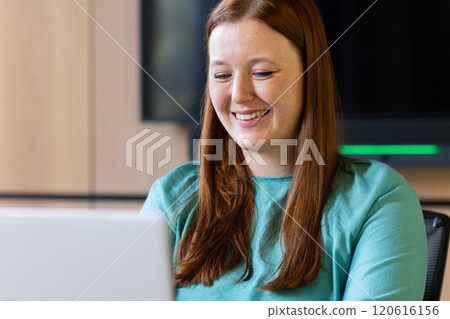 Smiling woman working on laptop in office, focusing on business tasks Smiling woman working on laptop in office, focusing on business tasks 120616156