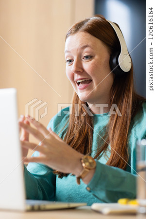 At office, Wearing headphones, woman video on video call on laptop, engaging in remote work At office, Wearing headphones, woman video on video call on laptop, engaging in remote work 120616164