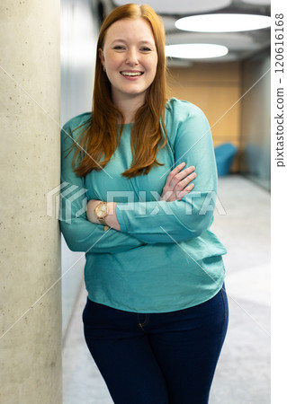 Smiling woman in business casual attire standing with arms crossed in office 120616168