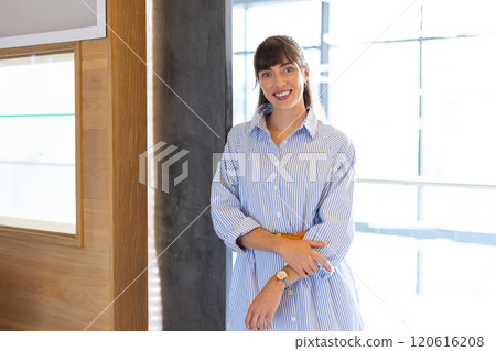 Smiling woman in striped shirt standing confidently in modern office setting 120616208