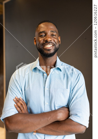 Smiling african american man in blue shirt standing with arms crossed, looking confident 120616227