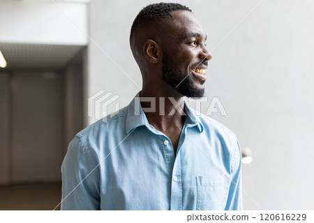 Smiling african american man in blue shirt looking away, standing indoors, feeling happy 120616229