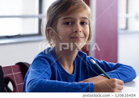 In school, smiling boy writing with pencil in classroom, looking at camera 120616484
