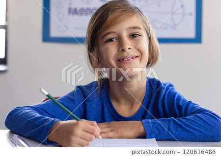 In school, smiling boy holding pencil and writing in classroom In school, smiling boy holding pencil and writing in classroom 120616486