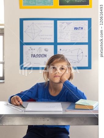 In school, boy sitting at desk daydreaming with books and papers In school, boy sitting at desk daydreaming with books and papers 120616493