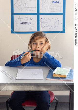 In school, boy sitting at desk thinking while holding pencil in classroom In school, boy sitting at desk thinking while holding pencil in classroom 120616496