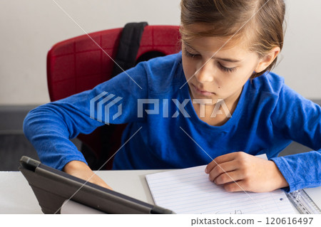 In school, boy writing in notebook while using tablet in classroom In school, boy writing in notebook while using tablet in classroom 120616497