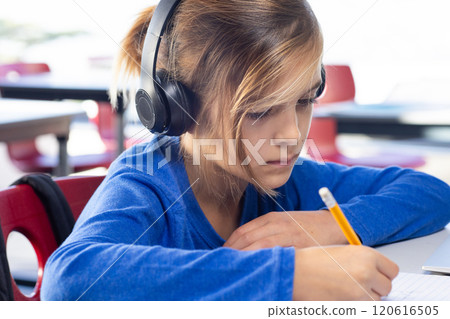 In school, boy wearing headphones writing with pencil, concentrating on work 120616505