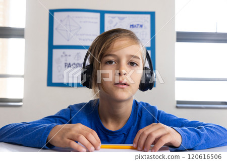 In school, boy wearing headphones and holding pencil, focusing on learning, on video call 120616506