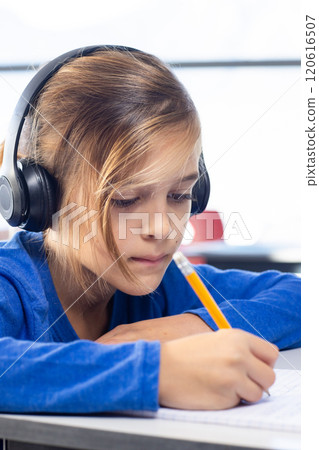 In school, boy wearing headphones writing with pencil, concentrating on work In school, boy wearing headphones writing with pencil, concentrating on work 120616507
