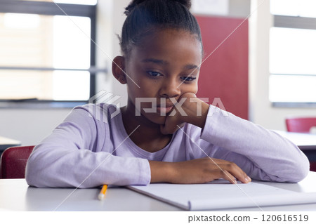 In school, african american girl sitting at desk looking at notebook, appearing thoughtful In school, african american girl sitting at desk looking at notebook, appearing thoughtful 120616519